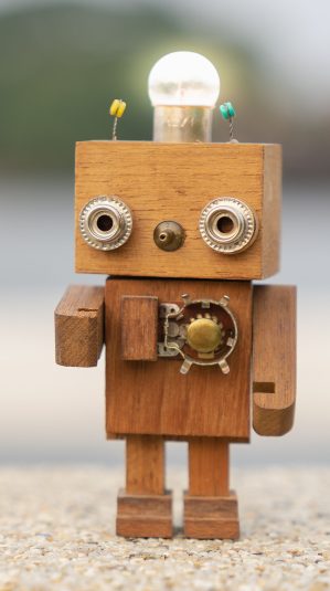 Retro wood robot with light bulb on the head standing on the table with blur nature background, nature and energy concepts.